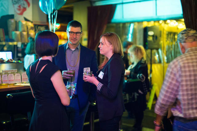 Guests mingling at the Love Bomb 2017 event, enjoying drinks and conversation, with festive decor and balloons in a lively atmosphere supporting My Voice Music nonprofit.